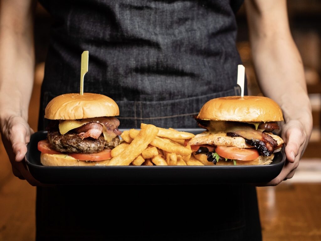 A waiter holding a trey with two burgers and fries at Cairns Burger Cafe