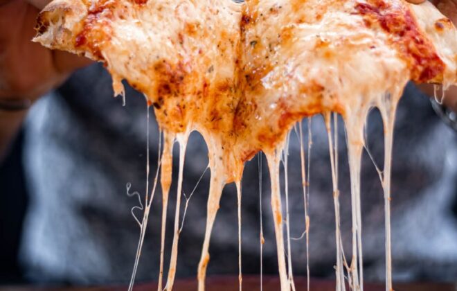 A guy in a plaid shirt picking up two slices of pizza with extra stringy cheese at La Pizza's Restaurant in Cairns.