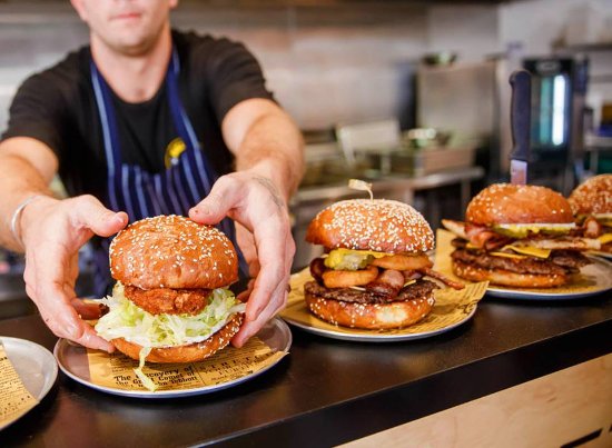 A variety of 4 burgers shown with the cook placing the fine burger on the plate at Hello Harry's.