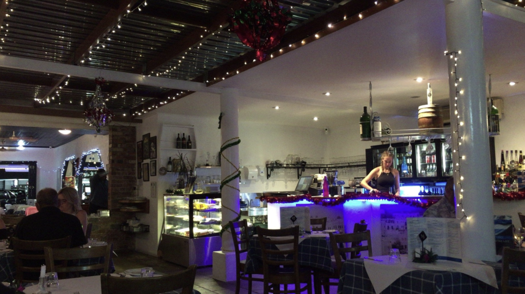 The inside view of Fetta's Greek Taverna with fairy lights and a girl behind the bar pouring a drink.
