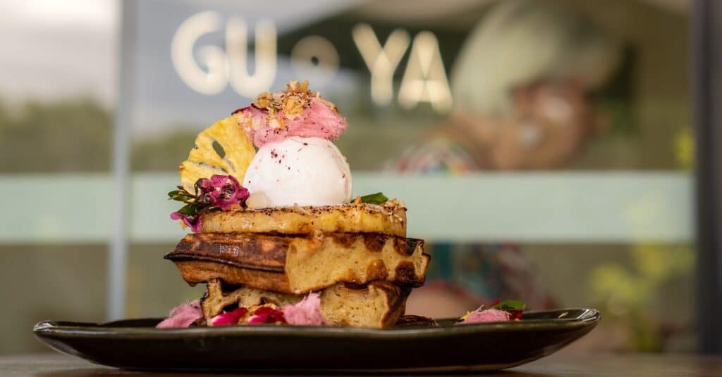 Guyala Cafe's Pina Colada Waffle stack with the Guyala neon sign in the background.